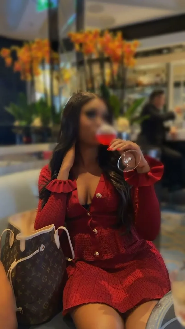 Short film of a woman in a red knit cardigan and skirt holding a pink drink at a lounge table.