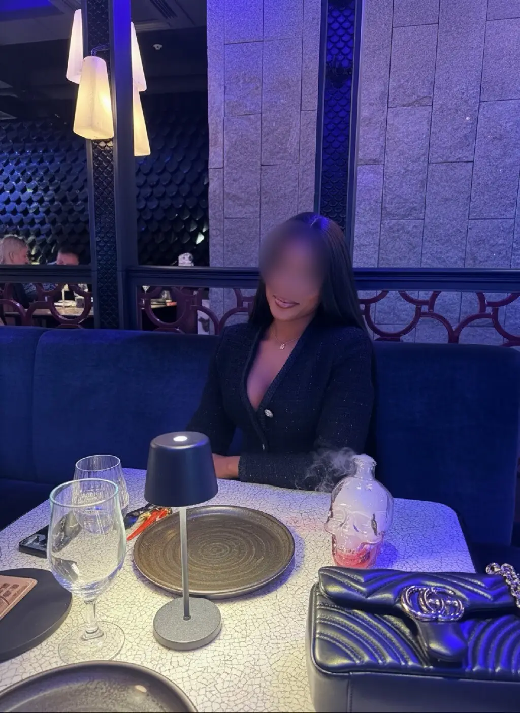Woman in a black tweed jacket seated at a restaurant table in a blue velvet booth.
